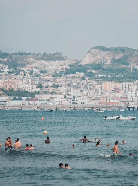 People swimming near Baia beach, Pozzuoli in Campi Flegrei, Italy. The Solfatara crater and fumarolic field are in the background